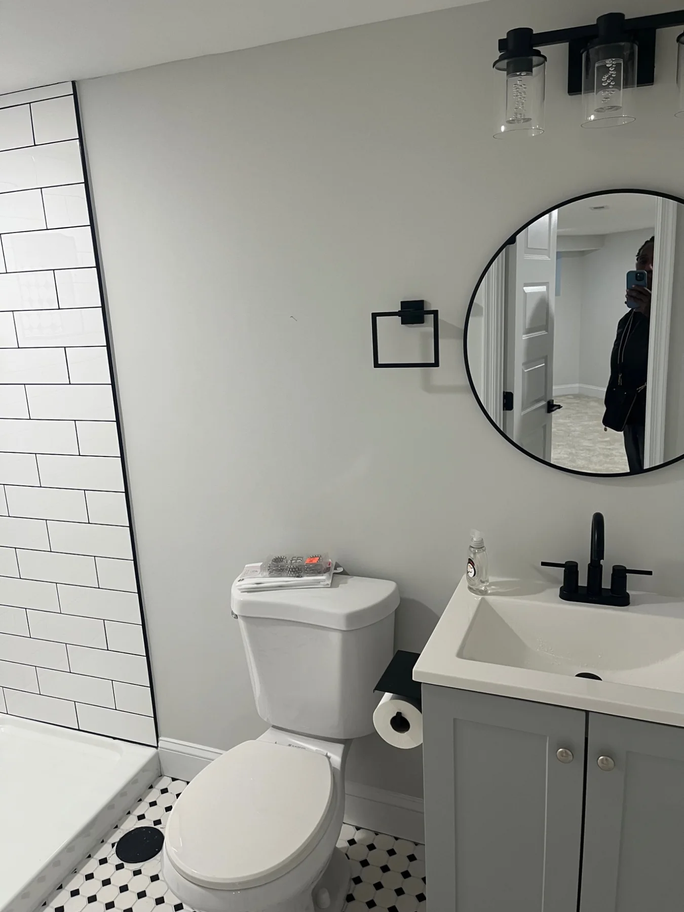 Completed bathroom remodel with gray vanity, black fixtures and round mirror